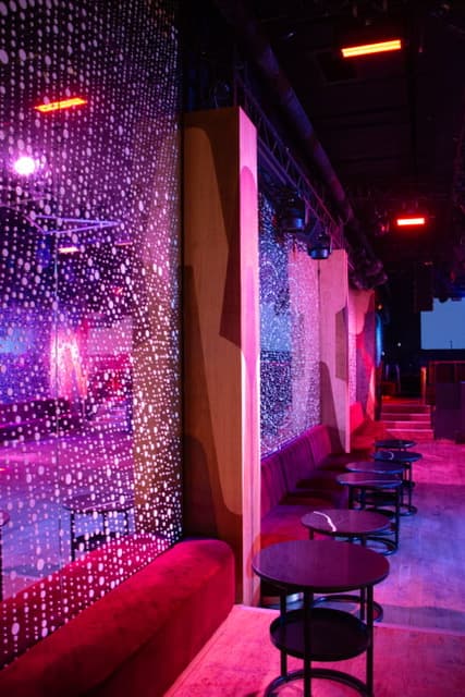 Espace lounge de club avec banquettes et éclairage néon violet.